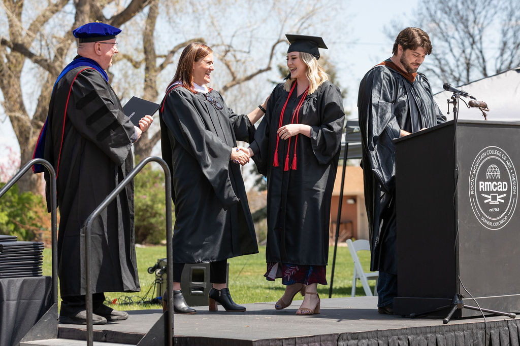 RMCAD student shaking hands and receiving her diploma on stage at graduation.
