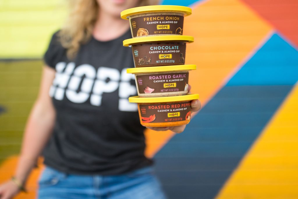 A woman wearing a Hope shirt holding four flavors of Hope Cashew & Almond Dip, packaging designed by EBD.