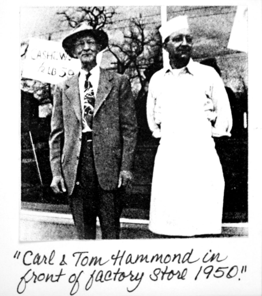 A historical photo of Carl and Tom Hammond, captioned "Carl & Tom Hammond in front of factory store 1950."